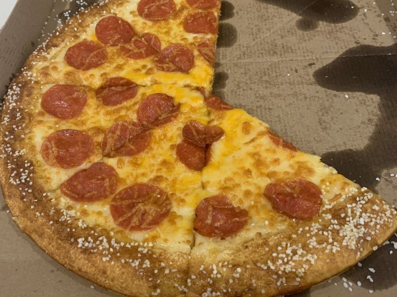 Photo of a pepperoni pizza with a pretzel crust, with salt. A few slices are missing, and it's in a greazy cardboard pizza box.