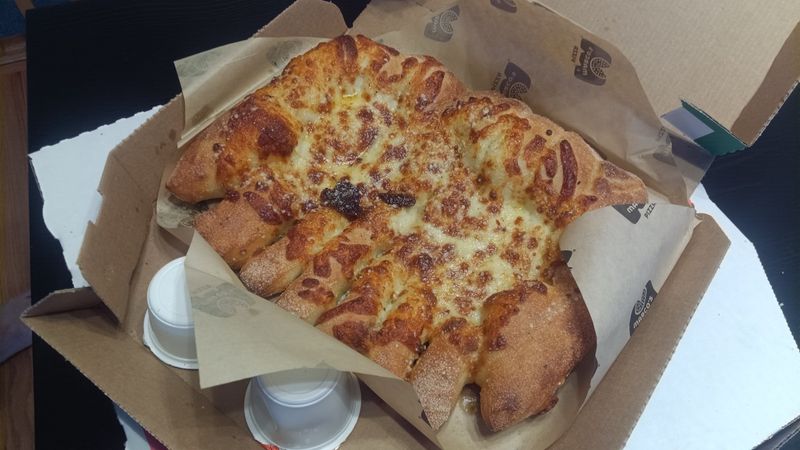 Photo of cheese bread on parchment paper in a cardboard box, with upside-down sauce cups.