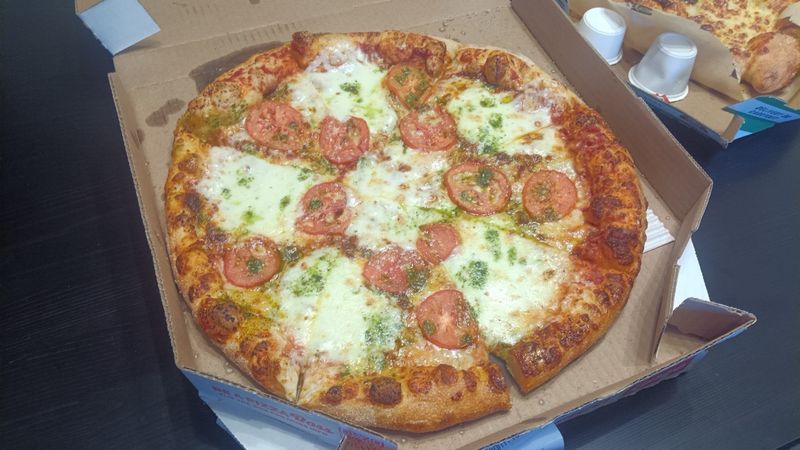 Photo of a margherita pizza, with lots of cheese, tomato slices, and basil, in a pizza box.