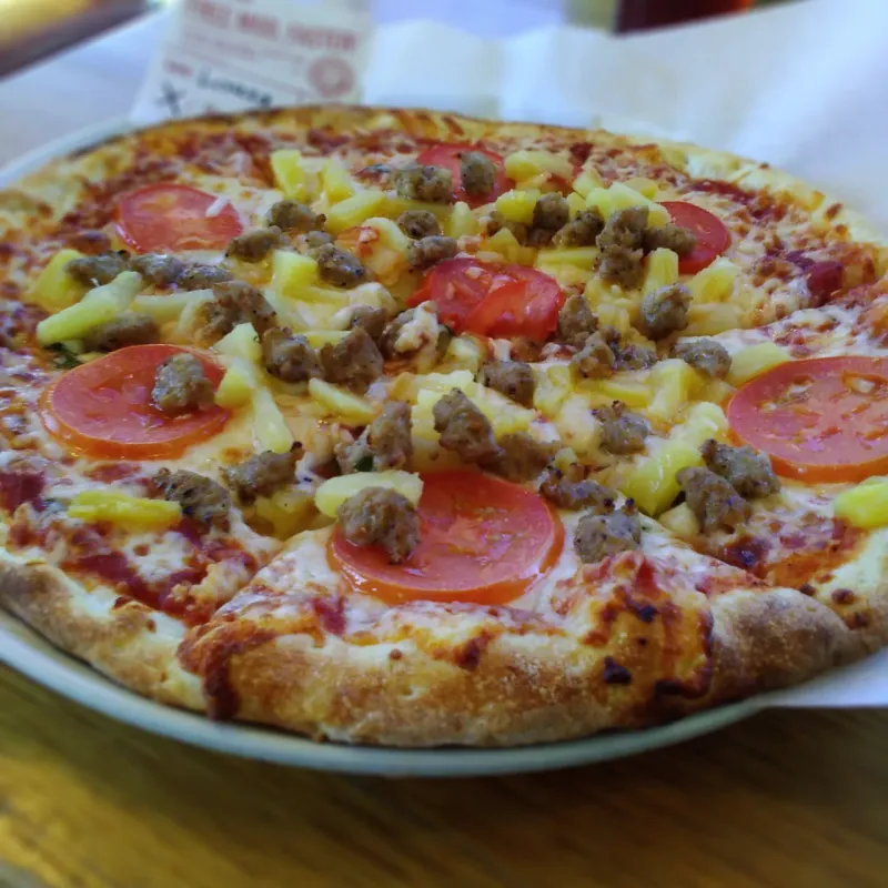 Photo of a pizza with pineapple, sausage, and tomatoes.