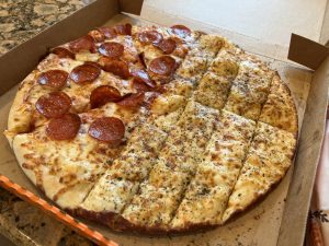 A pizza in the box, half is pepperoni pizza and half is cheese breadsticks.
